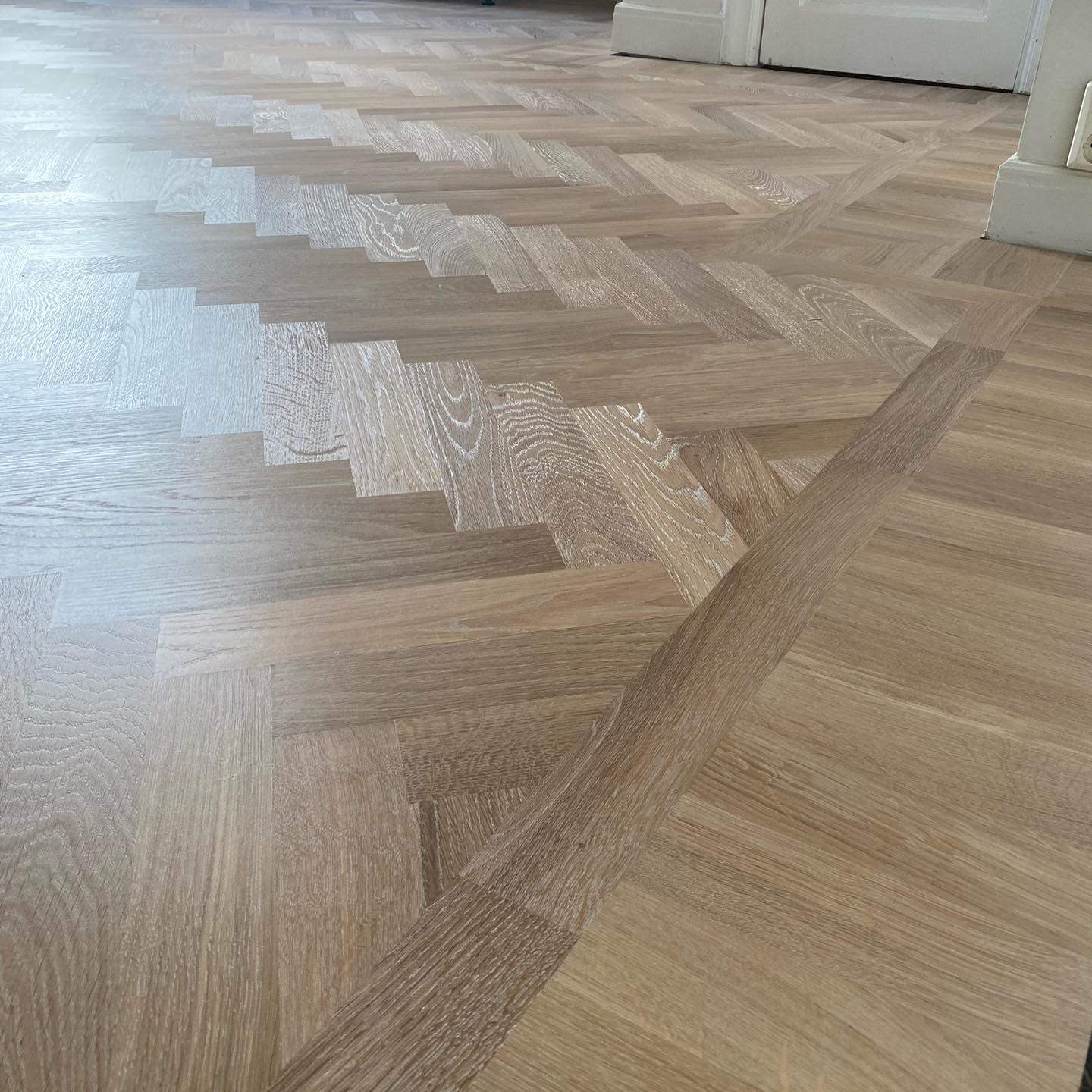 Närbild på massiv fiskbensparkett i ek med fris och ljus pigmentering som framhäver ådring och mönster.